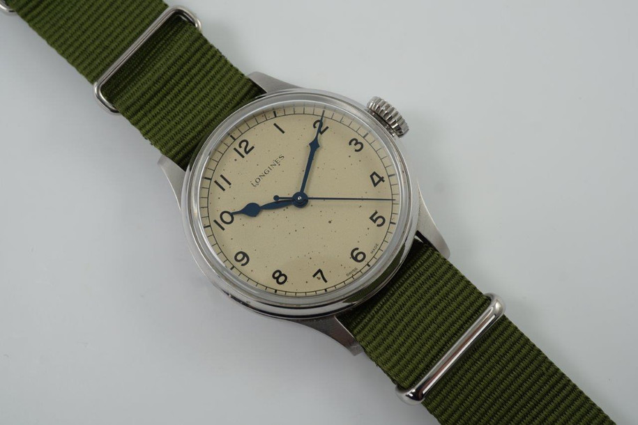 A fine Longines Heritage Military reference L2.819.4.93.2 in stainless steel. A 1940’s reissue of Longines’ enduring association to the realm of aviation brought this model, current in today’s catalogue of the Longines Heritage collection with US. Retail of $2425. Longines describes this dial color as silver, although it appears to be more beige with faint splattering of dots, bearing a patina-like impression of its vintage predecessor. The painted Arabic numerals and railroad ring for the minutes, typical of military pieces of its time. Wears handsomely on the wrist, and may be rotated with a Velle Alexander custom strap or military green nato-style strap, apropos to its theme.  

Original dial, blued steel hands and crown.
Case measures 38.5 x 47.6 mm, 11.70mm thick. 
Longines automatic movement.
Serial# 498242xx
Sapphire crystal.
New generic green 19mm Nato-style strap.
Extra long Velle Alexander custom strap, like new.
Longines 18mm steel signed buckle.
19mm lug width.