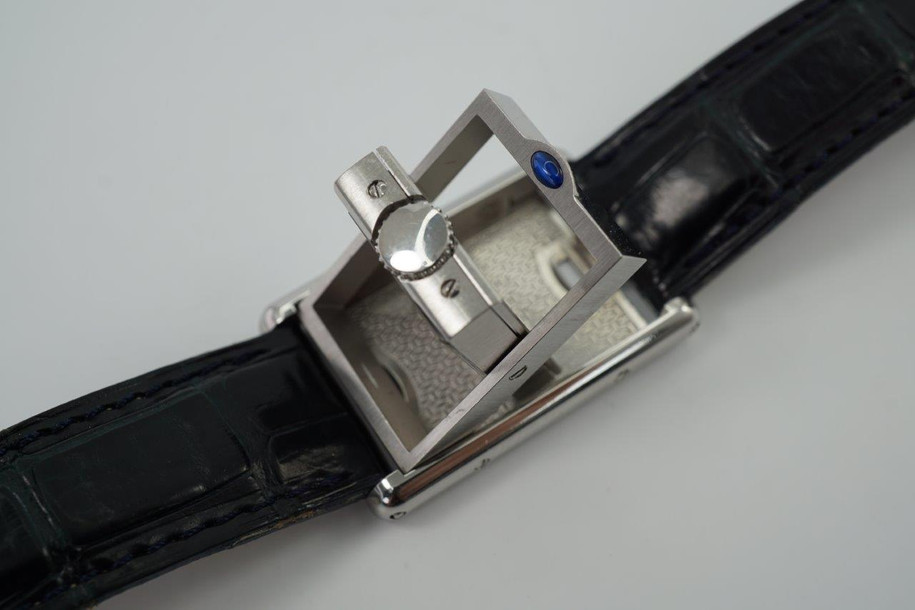 A nice preowned Cartier Basculante reference 2386 with Cartier papers, crafted circa 2001. This is a curious design modeled after their first Cabriolet model from 1932 for its intended functionality during physical activity, so that the crystal is protected, as such the crown placement is allocated to the 12 o’clock position with a horizontal blue oval cabochon charmingly sitting on top. The dial is the standard silvered dial with black Roman numeral markers and inner chemin de fer minute track, secret Cartier signature at 10 o’clock and blued-steel sword-shaped hands. The inner polished case housing said dial is configured into a swing frame, movable in either forward or reverse direction, revealing double C signatures on the inner case back and a smooth steel topper. While this function may not pertain to today’s needs, it is a fascinating detail that sets it apart from the regular Tank models and manages to sit relatively flush on the wrist.