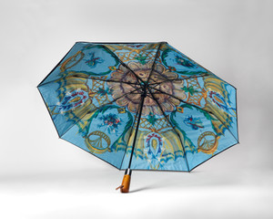 Open umbrella resting on a white surface with a multicolor print on the inside. Open umbrella resting on a white surface with a multicolor print on the inside.