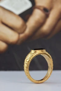 Gold ring with black onyx stone standing up in front of a backdrop of Sir Thomas More's fingers.