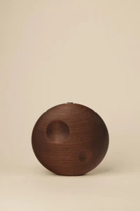 Closed, circular dark walnut wood handbag with two subtle crescent-shaped indentations, photographed against a neutral background.