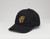 Black baseball hat with the embroidered gold Frick Collection logo on the front sitting on a white surface. Black baseball hat with the embroidered gold Frick Collection logo on the front sitting on a white surface.