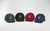 Four baseball caps in green, black, burgundy and navy, arranged in a curved line. Four baseball caps in green, black, burgundy and navy, arranged in a curved line.