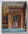Book cover showing the interior of a mansion. Two rooms are visible. The room closest to the viewer comprises of wooden walls and is decorated with a chandelier, antique furniture, ornaments and a portrait painting. The doors are open and lead to a room decorated with antique furniture and large scale paintings. Book cover showing the interior of a mansion. Two rooms are visible. The room closest to the viewer comprises of wooden walls and is decorated with a chandelier, antique furniture, ornaments and a portrait painting. The doors are open and lead to a room decorated with antique furniture and large scale paintings.