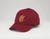 Burgundy baseball hat with the embroidered gold Frick Collection logo on the front sitting on a white surface.