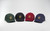 Four baseball caps in green, black, burgundy and navy, arranged in a curved line.