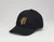 Black baseball hat with the embroidered gold Frick Collection logo on the front sitting on a white surface.