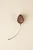 Back of a carved wood flower bud brooch showing the metal pin mechanism, the Frick Collection monogram, and Eittem's maker's mark, with a slender curved silver stem.