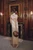 Model in a long cream dress carrying the sculptural walnut wood owl handbag by its integrated handle in an ornate wood-paneled room.