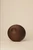 Back of a closed, circular dark walnut wood handbag with a subtle crescent-shaped indentation, photographed against a neutral background.
