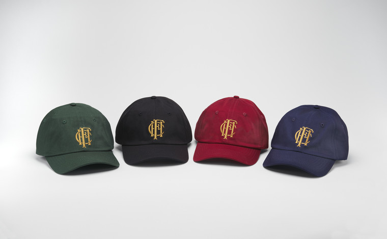 Four baseball caps in green, black, burgundy and navy, arranged in a curved line.
