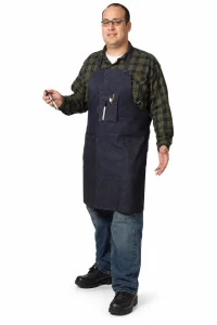 Worker wearing dark denim shop apron with tool pockets and safety glasses