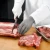 Chef wearing stainless steel butcher gloves while slicing meat in a professional kitchen