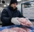 Cold-chain worker wearing insulated freezer gloves while handling frozen packaged meat in a refrigerated food processing warehouse.