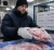 Cold-chain worker wearing insulated freezer gloves while handling frozen packaged meat in a refrigerated food processing warehouse.
