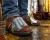 Worker wearing brown leather work boots with metal metatarsal guards on a wet industrial oil rig deck.
