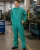 Factory worker wearing green industrial coveralls and safety glasses while standing near machinery in a manufacturing workshop.