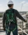 Worker wearing a green full-body fall protection harness, hard hat, gloves, and lanyard while standing on an elevated industrial rooftop platform.