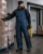 Cold storage warehouse worker wearing insulated freezer bib overalls, beanie, gloves, and work boots while handling frozen inventory near a freezer door