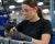 Woman wearing pink safety glasses and work gloves while using a pneumatic tool at an industrial assembly workstation