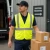 Courier wearing an ANSI solid fabric safety vest with Velcro closure while delivering boxes at a shipping and receiving dock