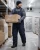 Cold storage worker wearing insulated freezer bib overalls, thermal jacket, gloves, beanie, and work boots while carrying boxes in a freezer warehouse.