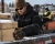 Worker wearing insulated winter work gloves and cold-weather PPE while handling lumber in a snowy outdoor industrial yard