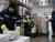 Cold storage workers wearing hi-vis insulated freezer gloves and cold-weather PPE while moving frozen boxes and operating a pallet jack in a freezer warehouse