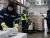 Cold storage workers wearing hi-vis insulated freezer gloves and cold-weather PPE while moving frozen boxes and operating a pallet jack in a freezer warehouse