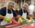 Candy production workers wearing green heat-resistant gloves, hair nets, safety glasses, and aprons while stretching taffy on a stainless steel worktable.