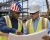 Black foreman wearing a patriotic American flag hard hat and hi-vis vest reviewing construction blueprints with an architect at an active jobsite.