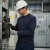 Electrical worker wearing a navy ARC 2 FR antistatic crewneck shirt, hard hat, safety glasses, and gloves while working near an industrial electrical panel.