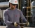 Industrial worker wearing a gray FR base layer shirt, hard hat, safety glasses, and gloves while working with equipment in an industrial facility.