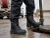 Worker wearing black waterproof work boots on a wet industrial jobsite near an open manhole access point