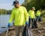Workers wearing hi-vis long sleeve safety shirts while cleaning up litter along a river shoreline