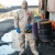 Worker wearing DuPont Tychem 5000 tan hooded coverall with gloves and respirator in hand