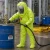 Worker wearing a lime chemical protective suit with hood, visor, gloves, and smooth over-shoe covers while handling hazardous materials in an industrial plant