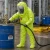 Worker wearing a lime chemical protective suit with hood, visor, gloves, and smooth over-shoe covers while handling hazardous materials in an industrial plant