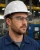 Industrial worker wearing clear safety glasses, white hard hat, and blue work shirt in a manufacturing facility.