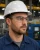 Industrial worker wearing clear safety glasses, white hard hat, and blue work shirt in a manufacturing facility.