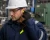 Worker inserting corded foam earplugs while wearing a hard hat and safety glasses in a factory