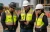 Three construction workers wearing hi-vis surveyor safety vests while reviewing a tablet on an outdoor jobsite