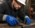 Worker wearing blue Tuff-Cor cut and puncture resistant gloves while handling metal bars in an industrial workshop.