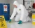Worker wearing a white chemical protective coverall, safety glasses, and gloves while cleaning a chemical spill near a spill kit in an industrial facility