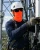 Telecom tower worker wearing an orange neck gaiter, white hard hat, safety sunglasses, gloves, and fall protection harness while servicing antenna equipment