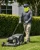 Outdoor lawn care worker wearing a hi-vis yellow neck gaiter, cap, sunglasses, gloves, and long-sleeve shirt while mowing grass in sunny conditions