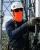 Telecom tower worker wearing an orange neck gaiter, white hard hat, safety sunglasses, gloves, and fall protection harness while servicing antenna equipment