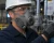 Industrial worker wearing a half-mask respirator with gray filter cartridges, hard hat, safety glasses, and hi-vis vest in a manufacturing facility