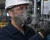Industrial worker wearing a half-mask respirator with gray filter cartridges, hard hat, safety glasses, and hi-vis vest in a manufacturing facility