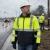 Worker wearing ANSI Class 3 hi-vis bomber jacket at a wet roadside jobsite